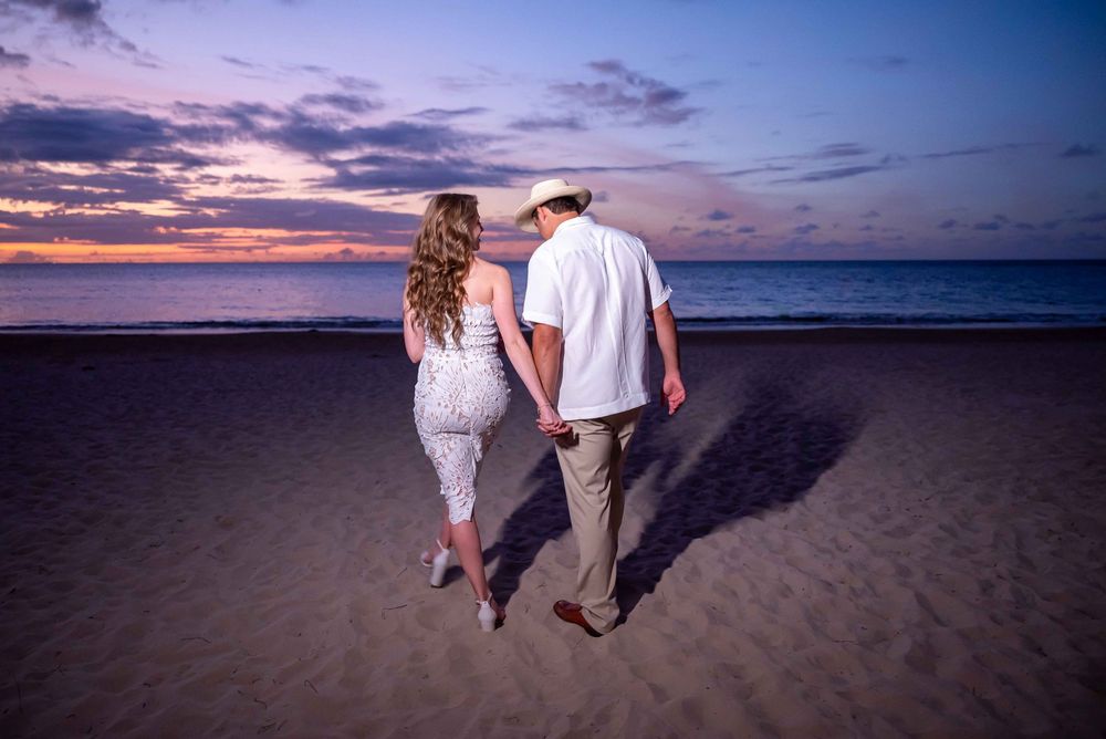 Couple walking on beach at sunset casting long shadows in the sand.
