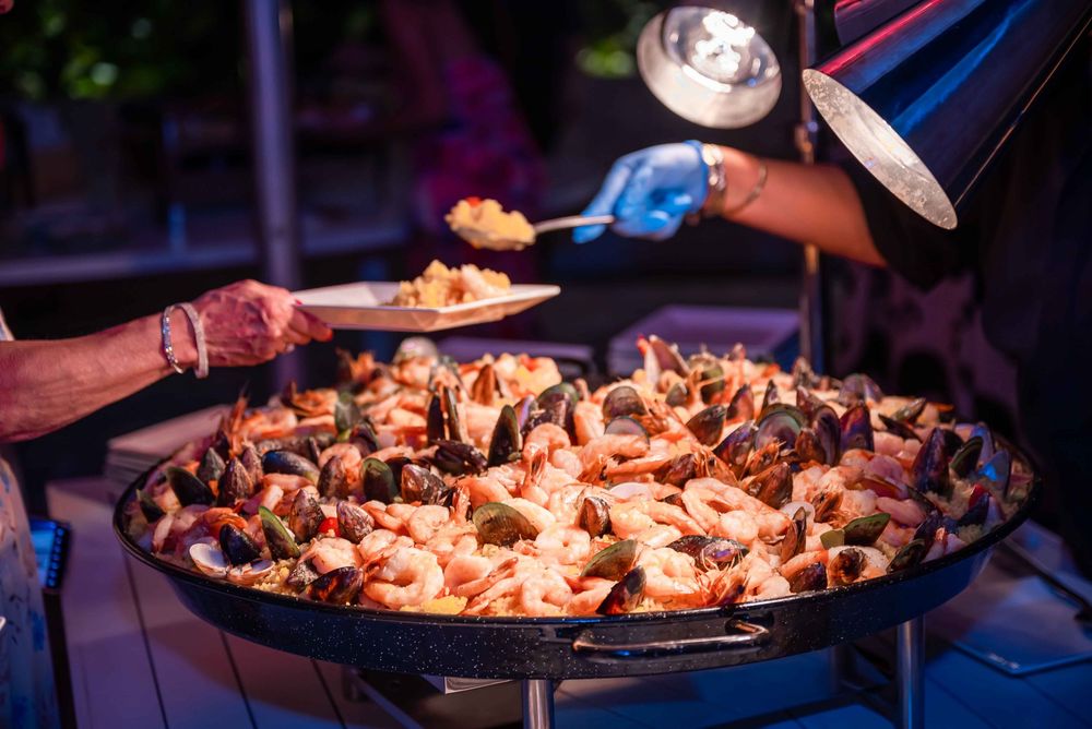 Large pan of seafood being served at nighttime outdoor event.