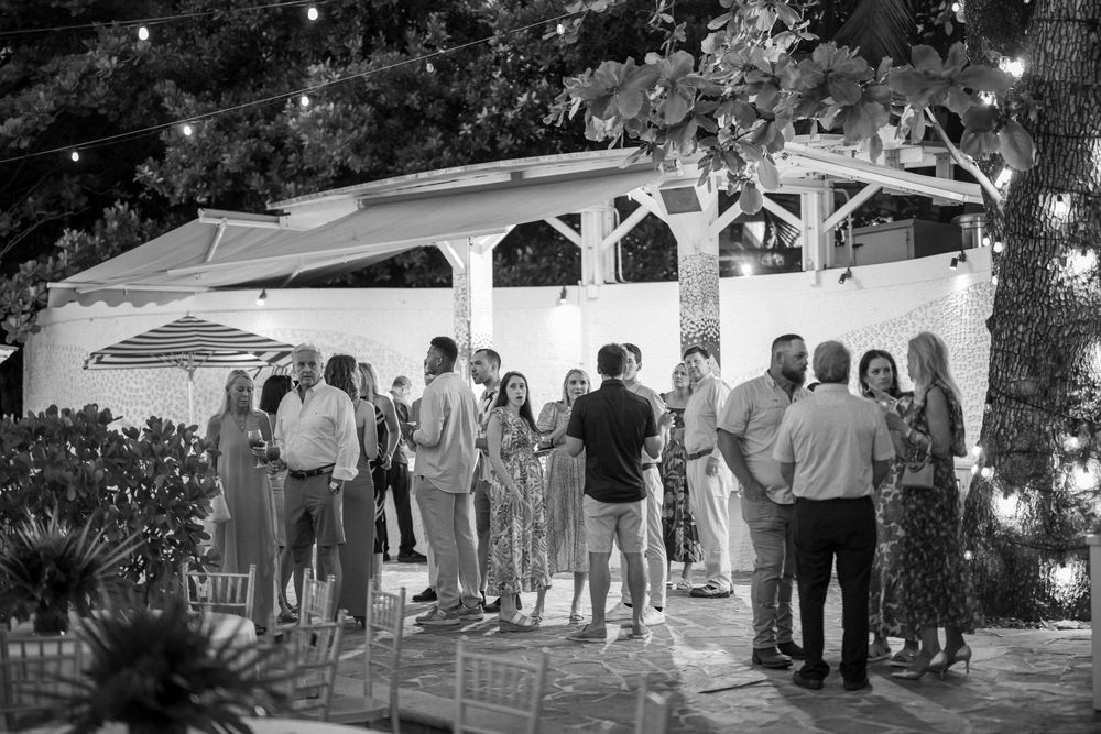 Black and white photo of guests gathering at outdoor evening reception under covered pavilion.