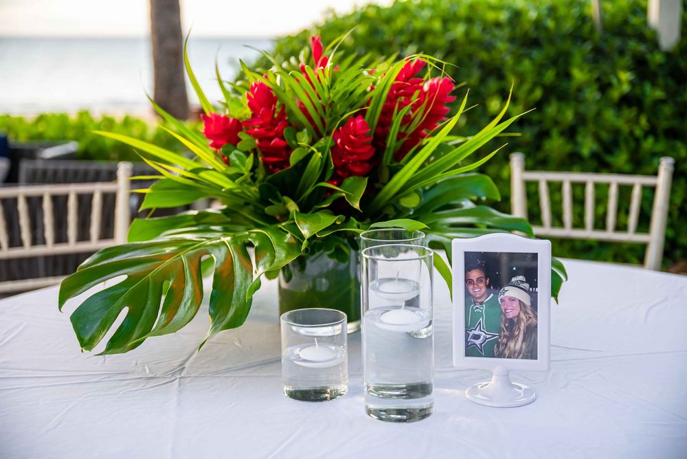 Formal table settings with red tropical floral centerpieces and framed photos.