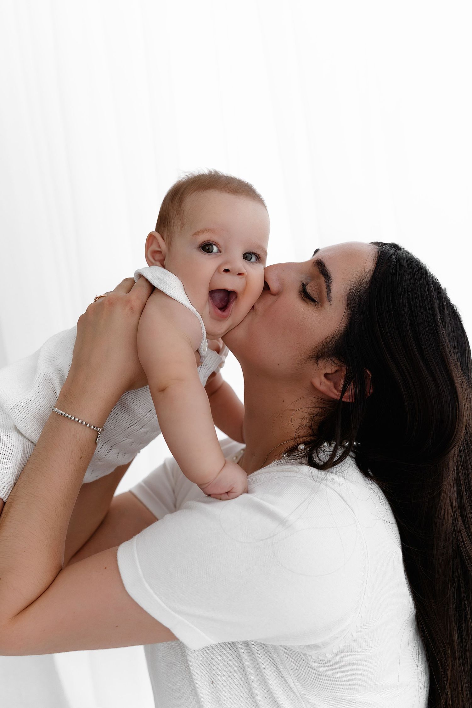 A tender moment between parent and baby shows affection and joy against a white background.