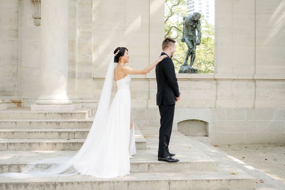 A bride and groom share a first look moment on elegant stone steps near classical columns.