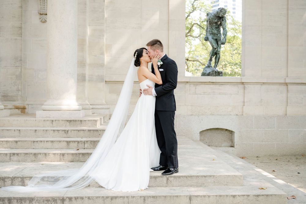 An elegant wedding couple shares an intimate moment on marble steps between grand white columns of a classic building.