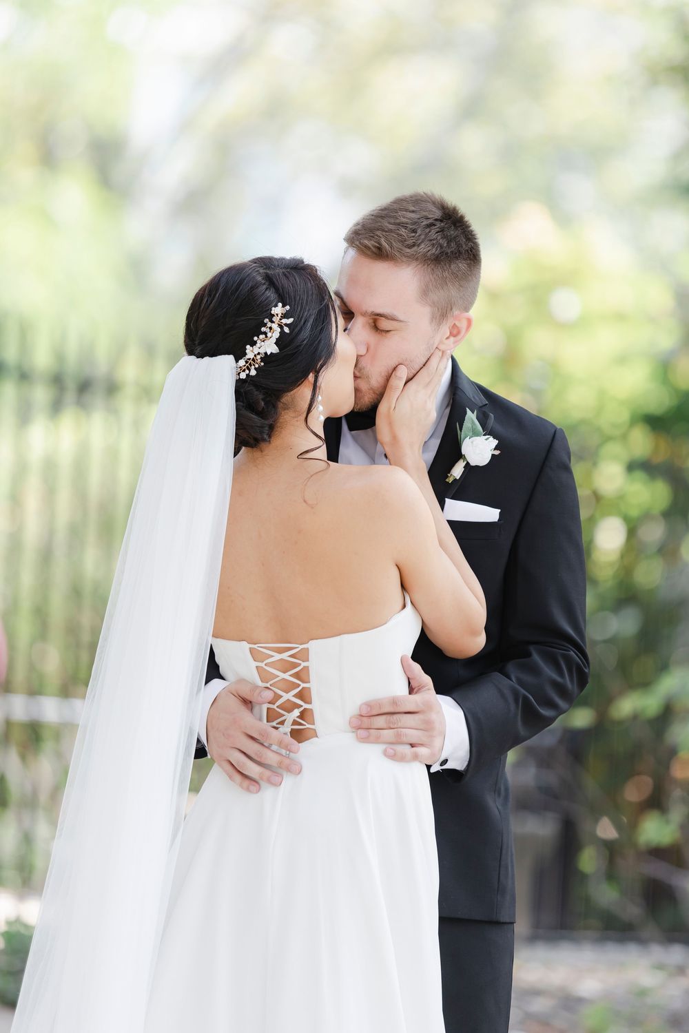 A romantic wedding kiss between a bride in a lace-up dress and groom in black suit amidst a garden setting at Philadelphia's Rodin Museum