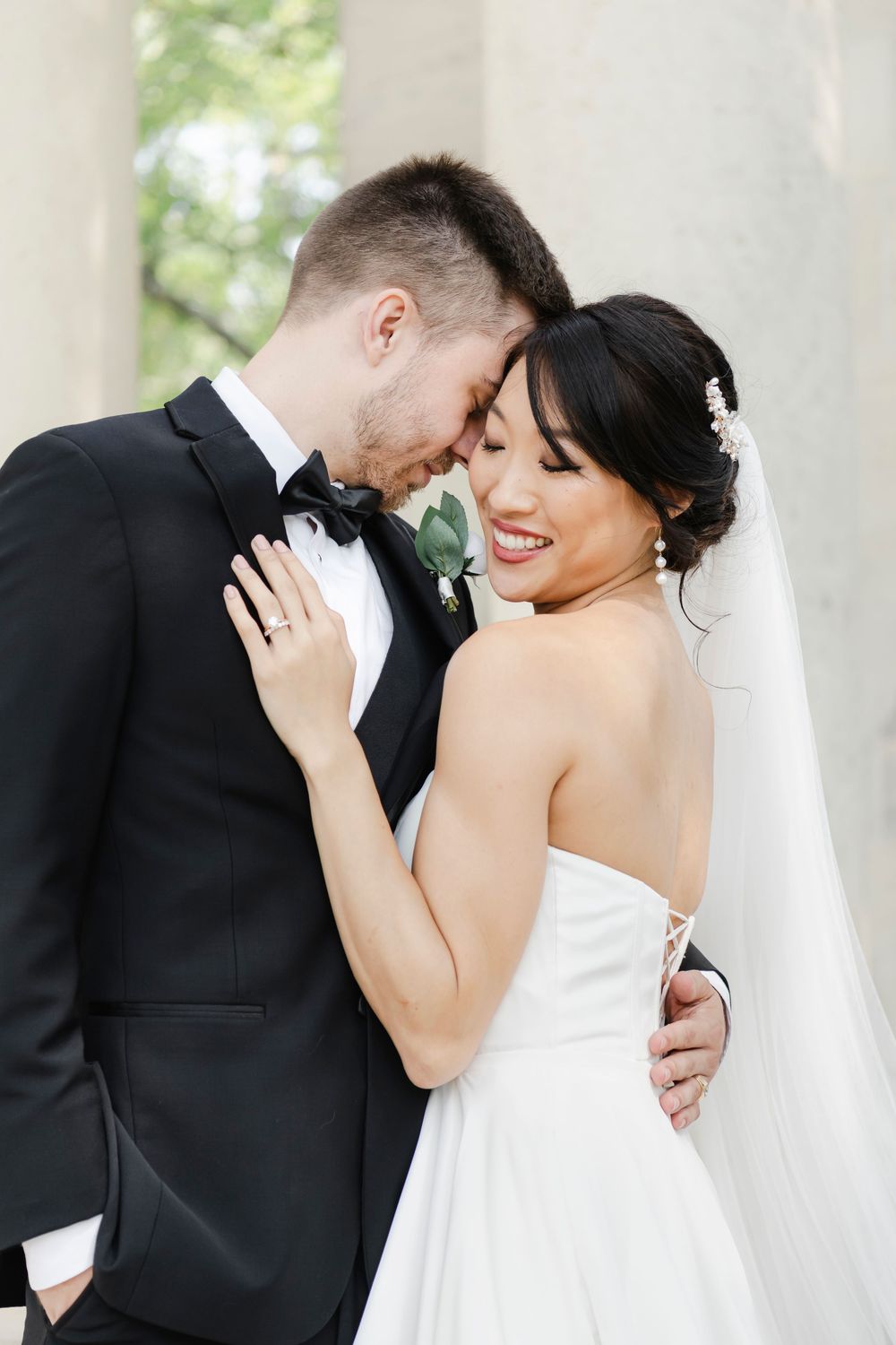 A happy couple shares an intimate moment on their wedding day, with the bride in white and groom in black tuxedo.