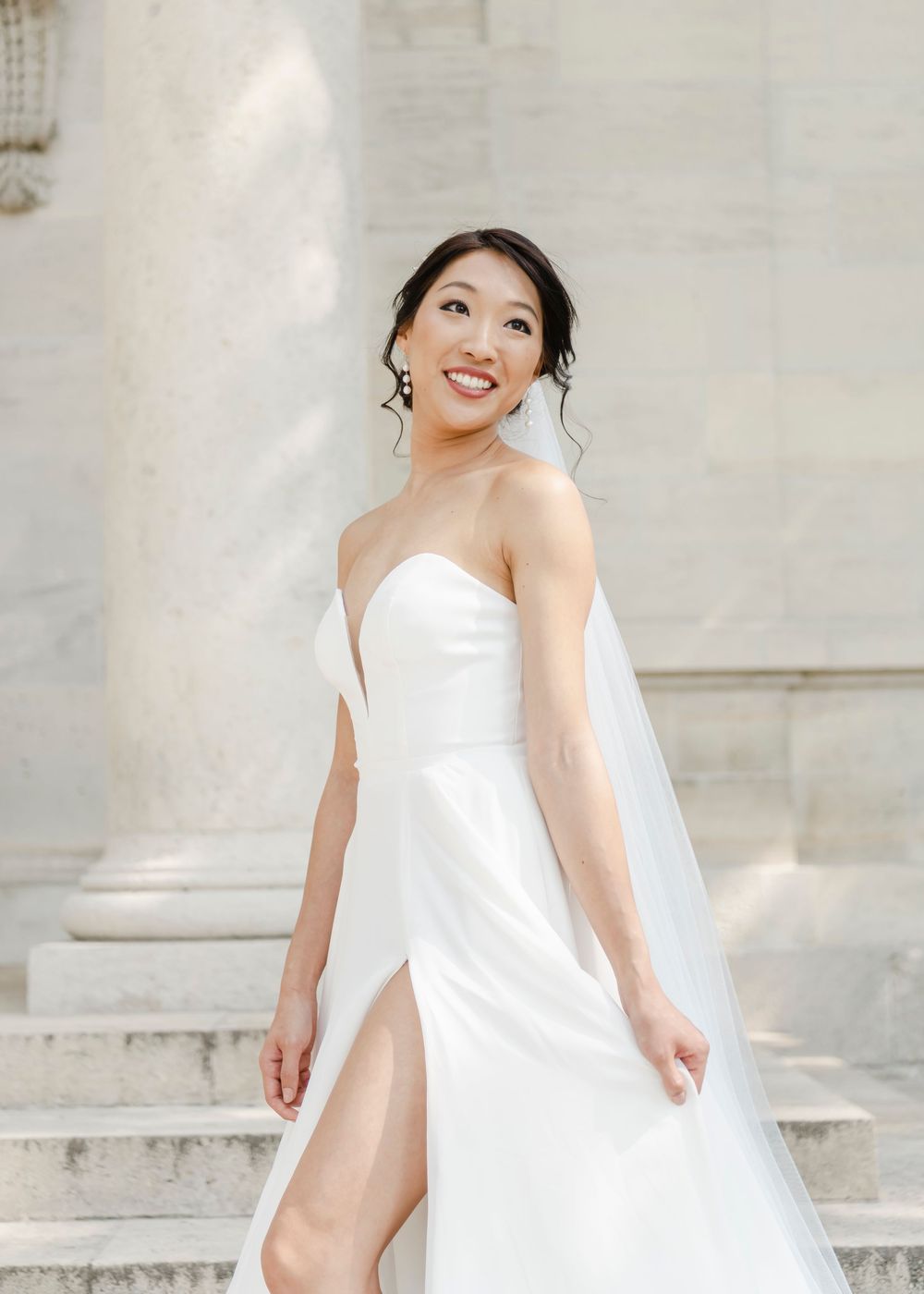 A bride in a stunning white strapless wedding gown with a thigh-high slit poses elegantly on stone steps.