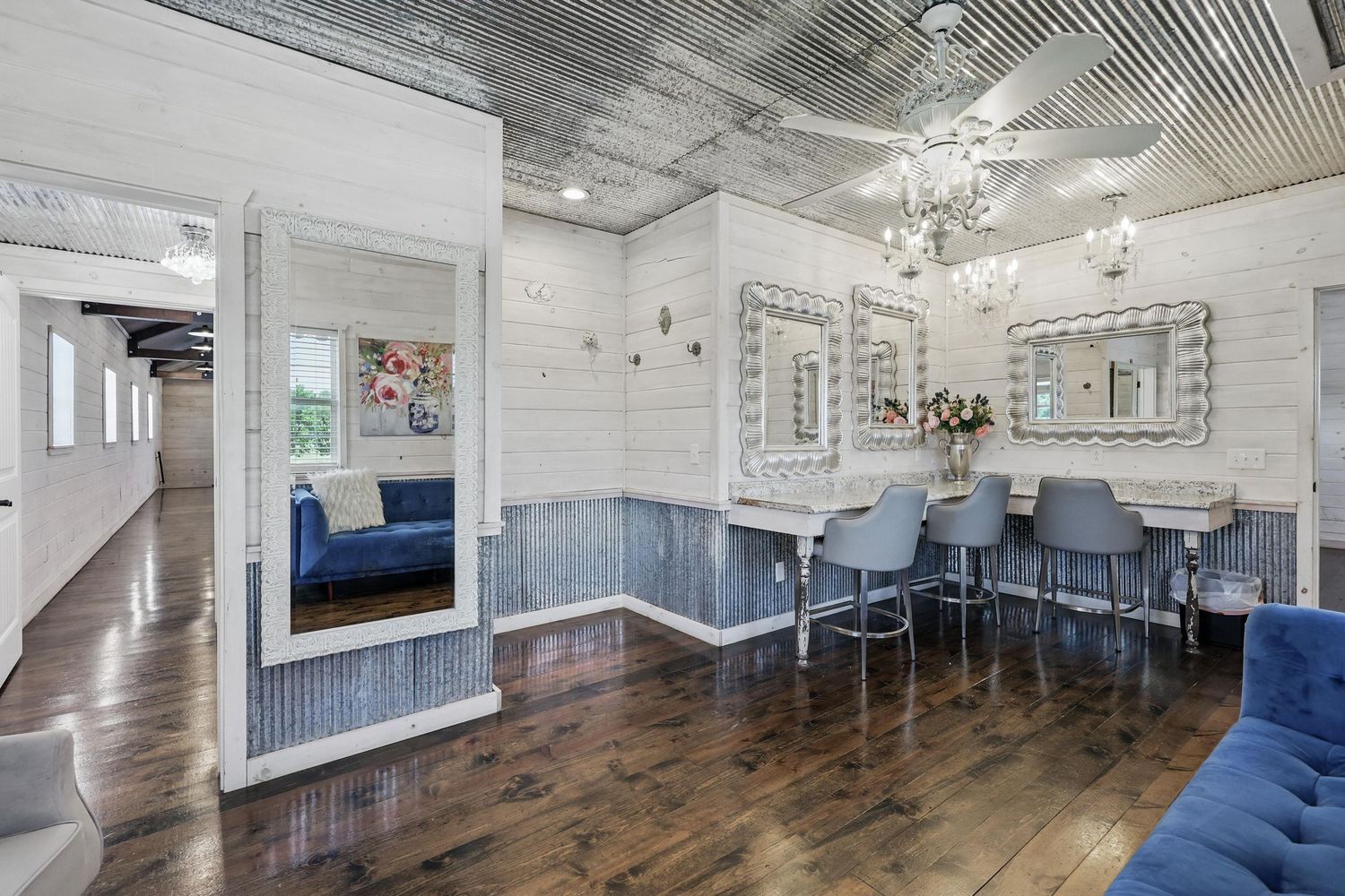 Modern dining room with blue banquette seating, grey chairs, and chandelier in a white and grey interior with wood floors.