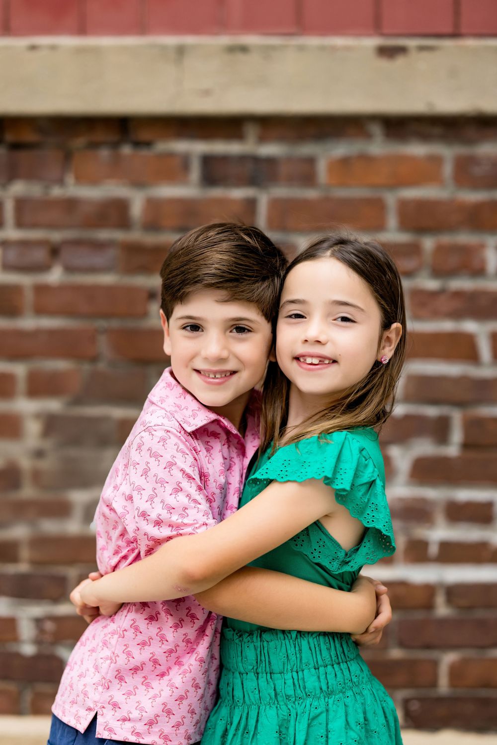 Sweet sibling embrace against rustic brick wall during summer photoshoot.
