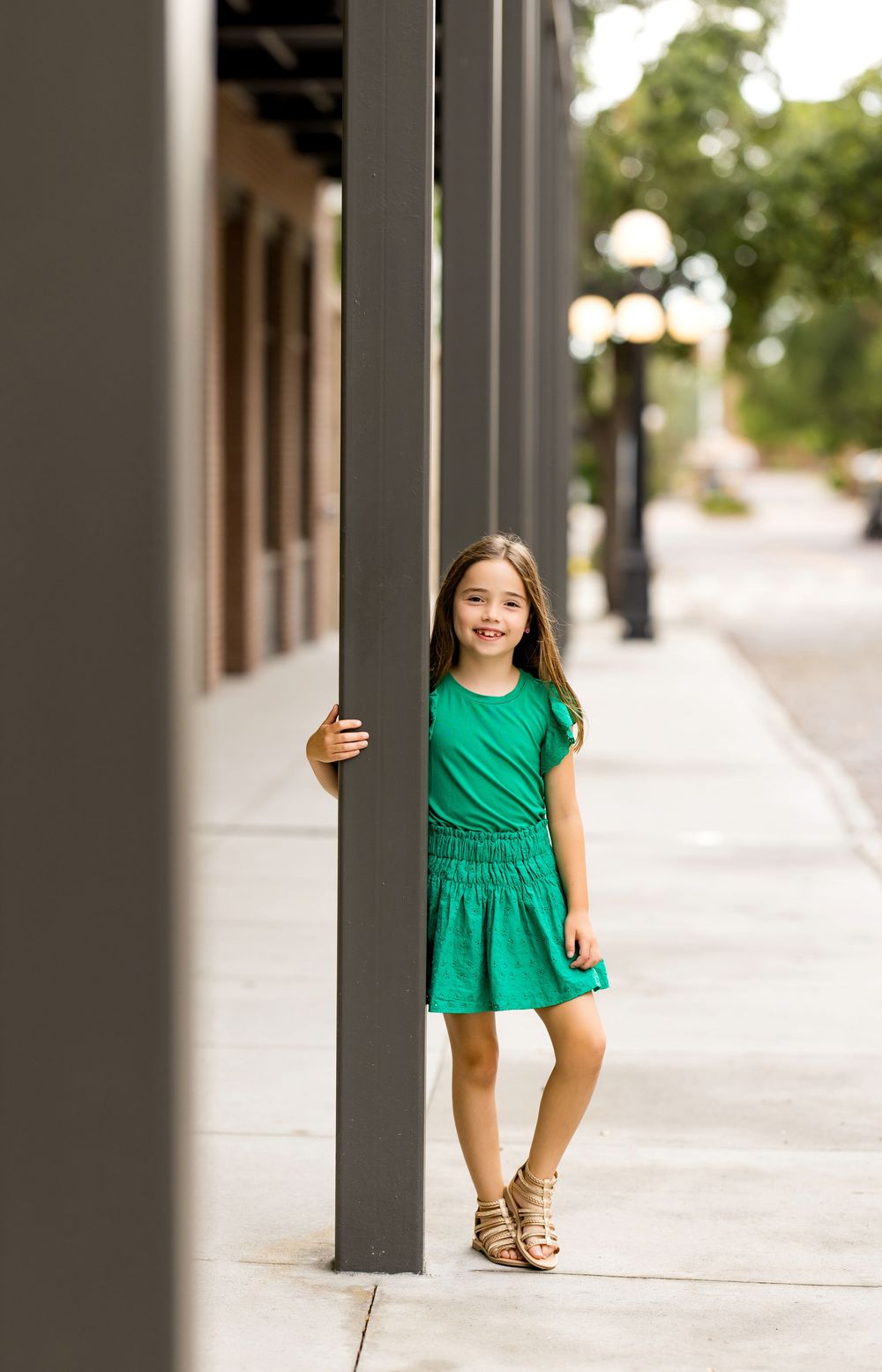 Child in green dress playing peek-a-boo behind brick columns.