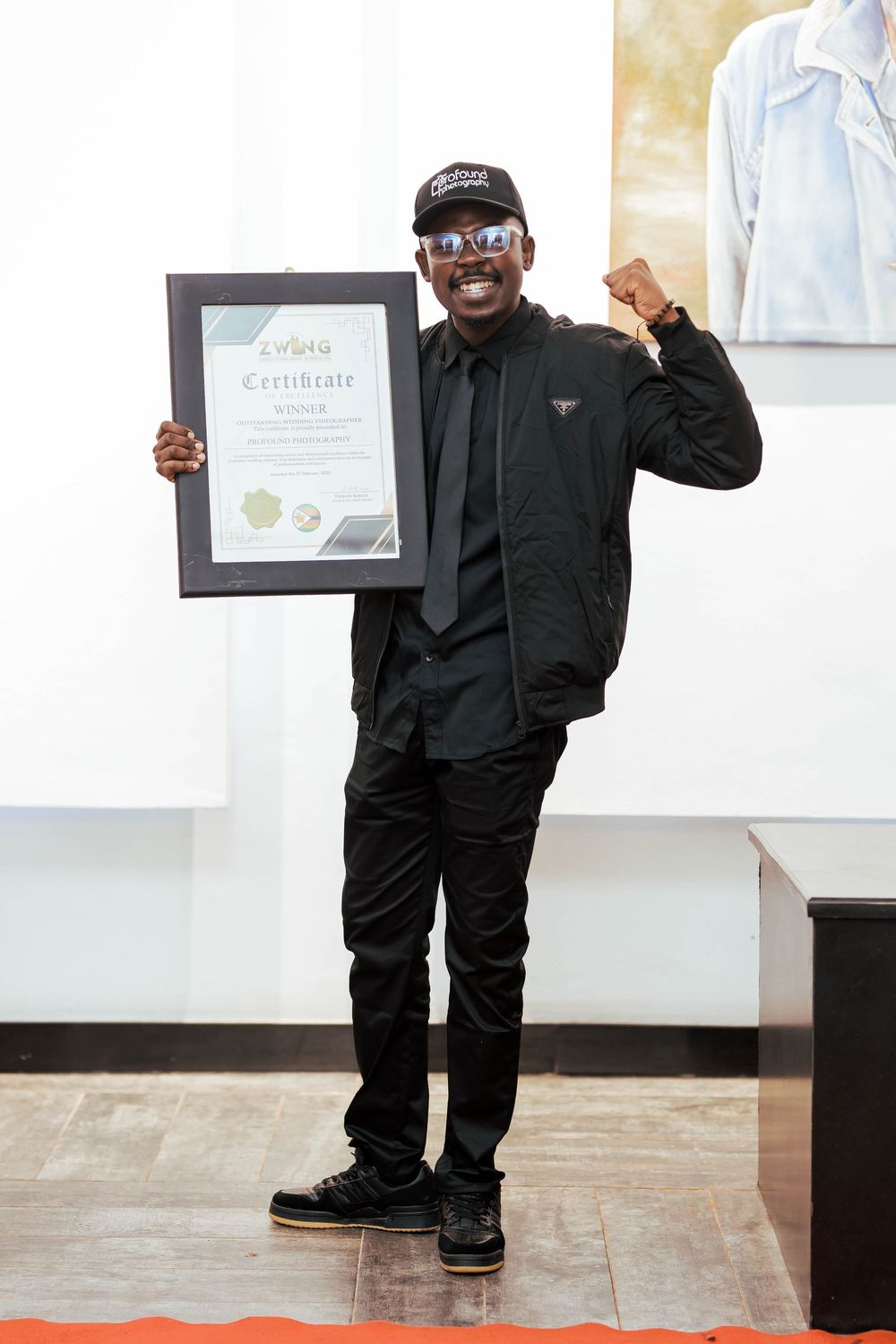 Person in all black attire holding up a framed certificate while making celebratory fist pump gesture.