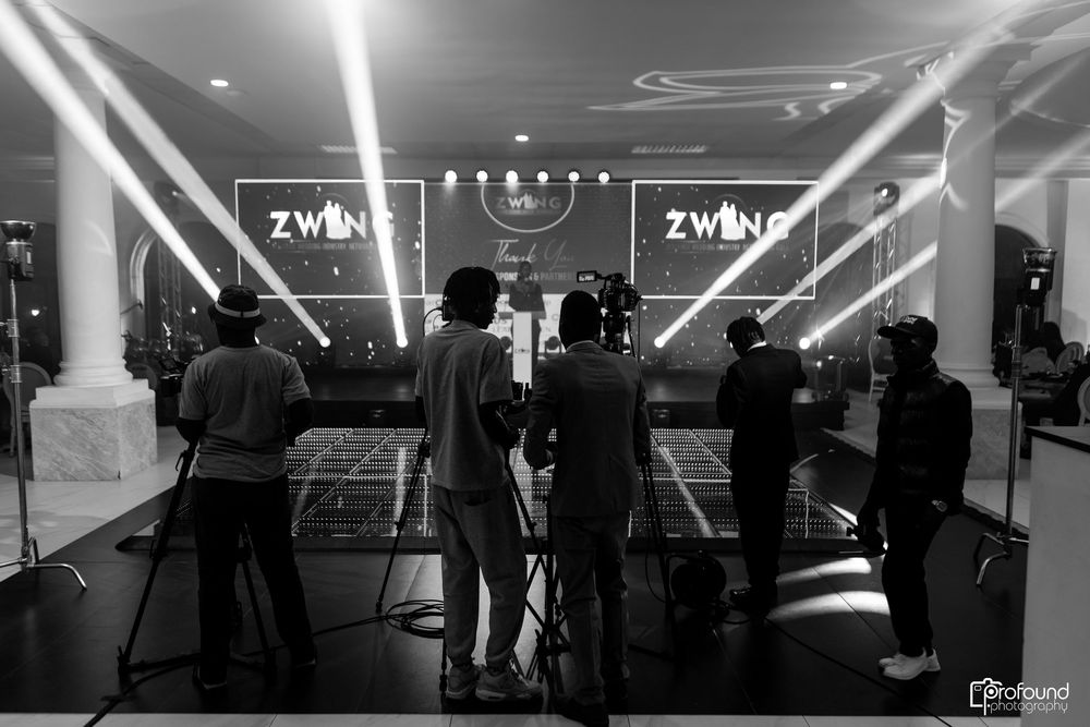 A black and white photo of people watching a stage with illuminated ZWMS signage and dramatic lighting beams.