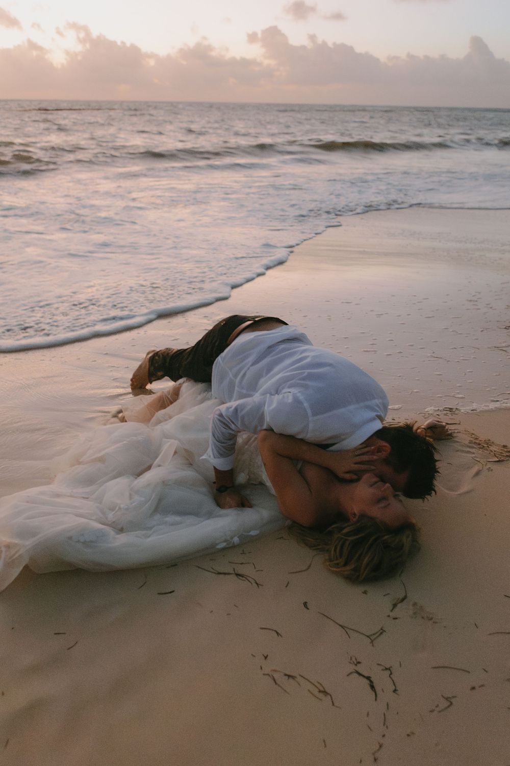 A dreamy beach scene at sunset with a flowing white dress on the sandy shore near gentle waves.