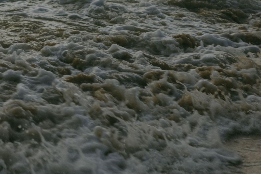 Turbulent ocean waves create a foamy white pattern against dark water in stormy conditions.