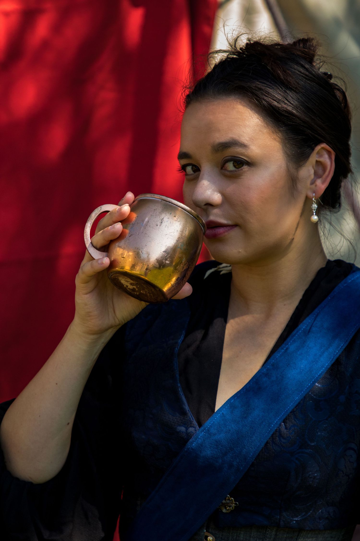 Person in blue and black garment holding a metallic copper-colored cup against a red backdrop.