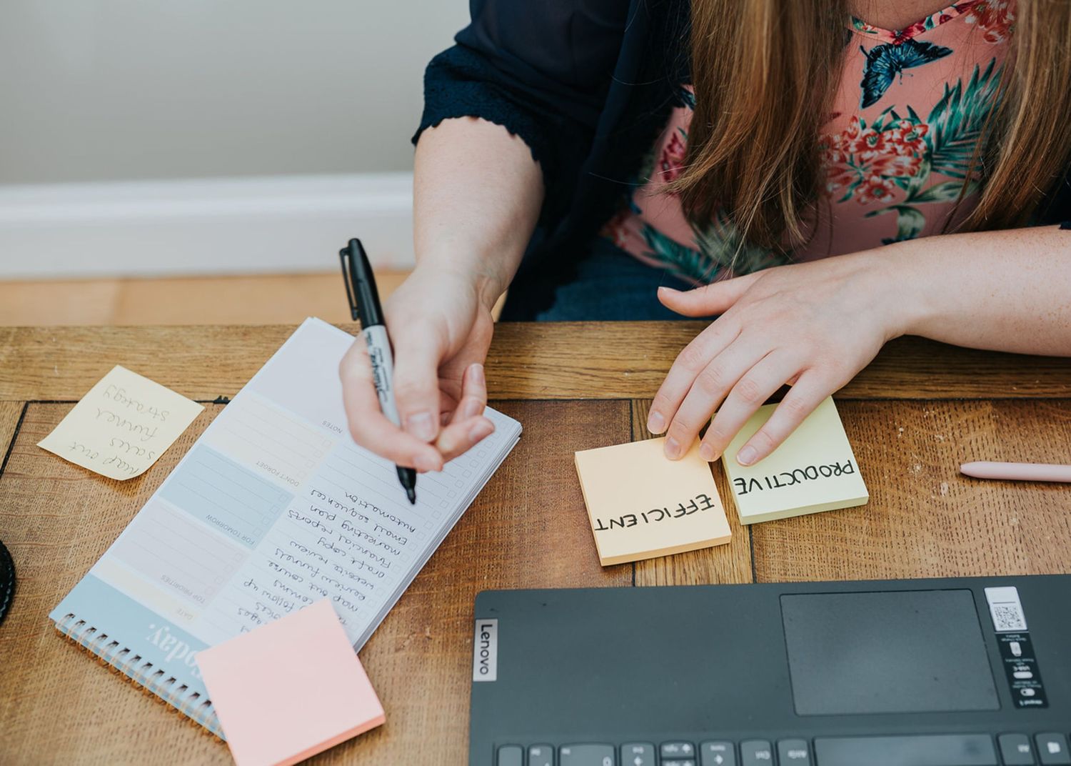 Person writing notes on sticky notes during a planning session at a wooden desk with laptop and office supplies.