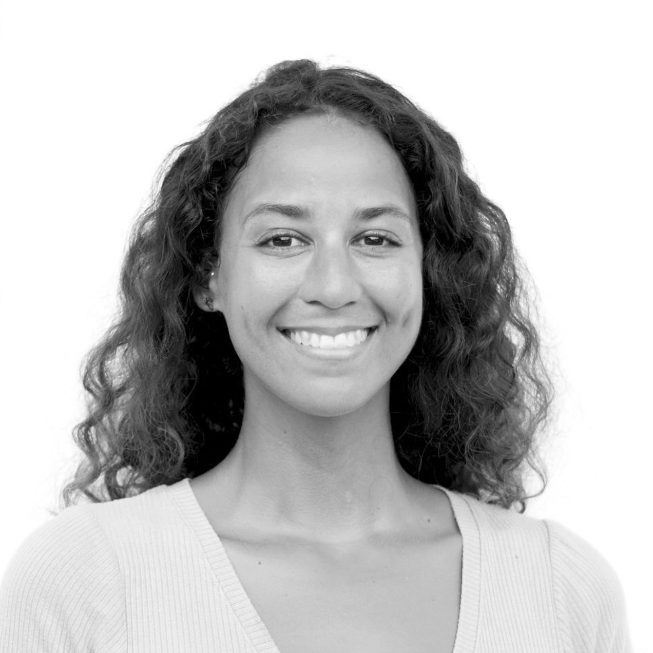 Black and white professional headshot of a person with curly hair and bright smile wearing a light colored top.