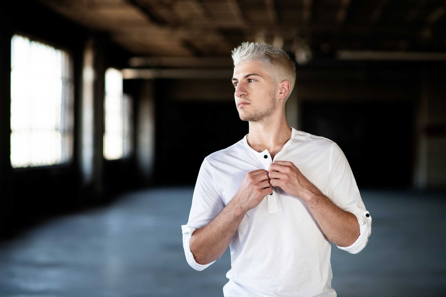 Young man in white shirt adjusting collar in empty warehouse setting.