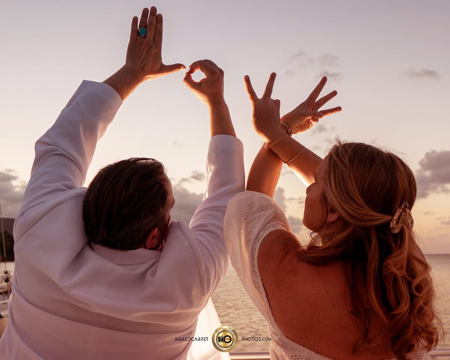 Wedding couple raises their hands joyfully against a sunset sky at the beach.