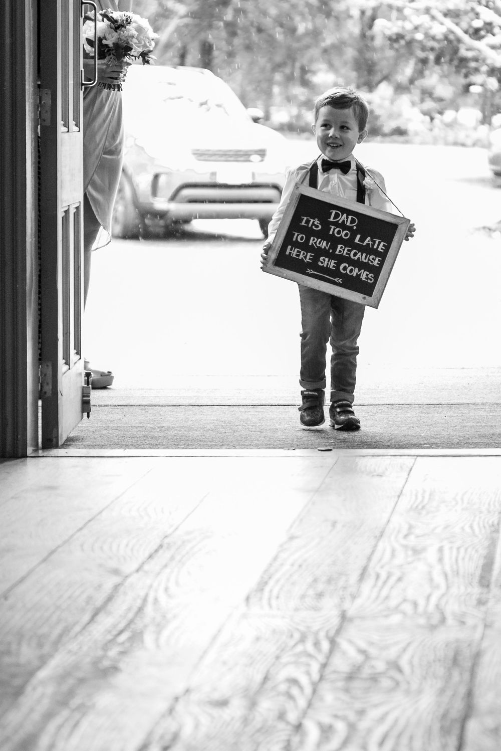 A young child holds a chalkboard sign in a black and white wedding day photo.