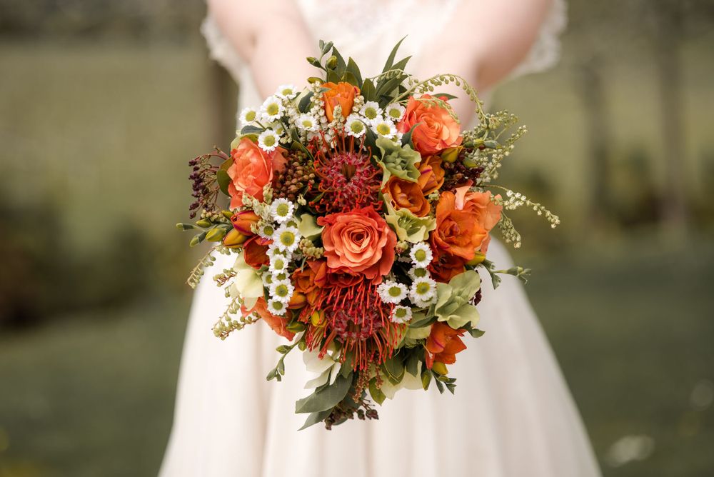 Detailed view of a fall wedding bouquet featuring coral roses, protea, and white wildflowers.
