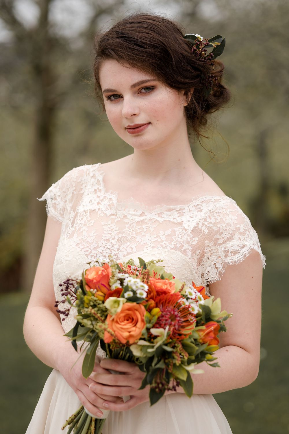Romantic bridal portrait featuring delicate lace cap sleeves and a vibrant coral floral bouquet.