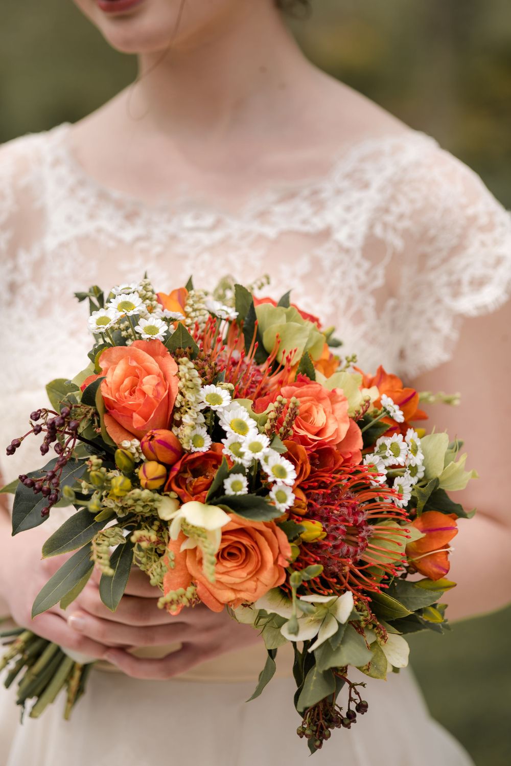 Close-up of coral and orange bridal bouquet with roses, daisies, and mixed wildflowers.