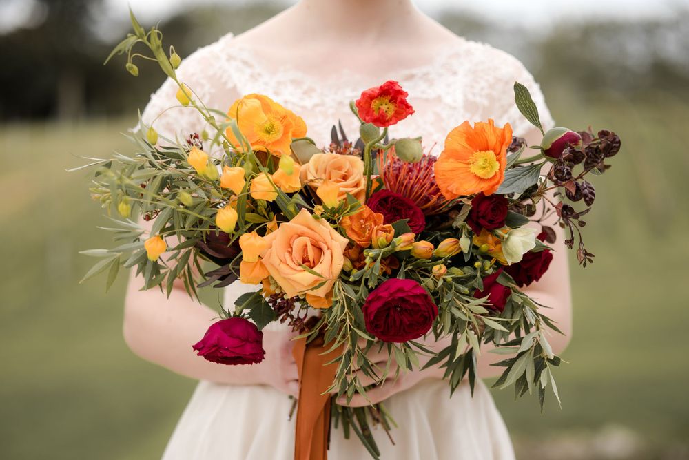 Vibrant autumn wedding bouquet with orange roses, red dahlias, and cascading greenery.