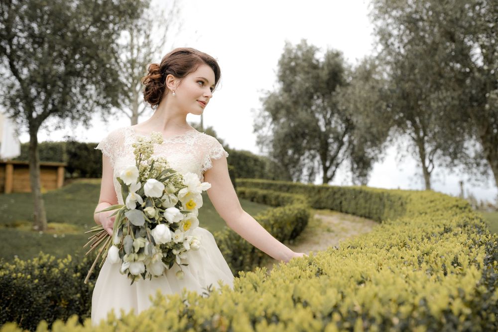 Ethereal bridal portrait in a flowing white dress amidst manicured garden hedges and olive trees.