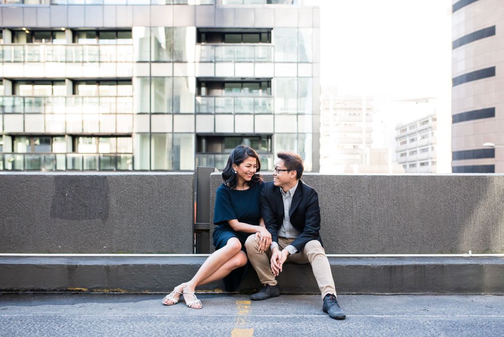 A couple sits casually on a modern rooftop terrace surrounded by urban architecture.