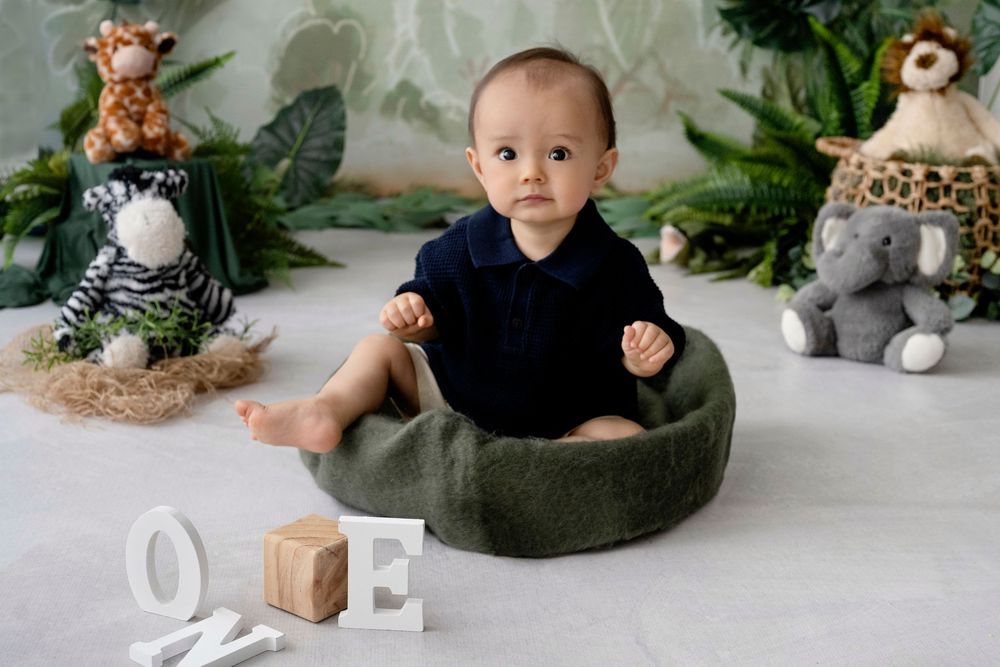 Baby in blue outfit sits on floor surrounded by jungle animals.