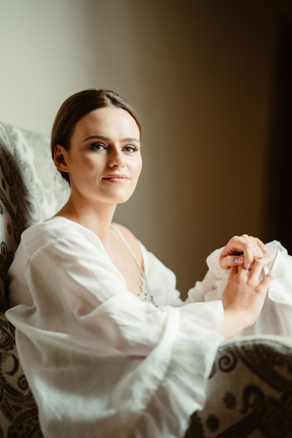 A bride in a white robe sits contemplatively during wedding preparations.