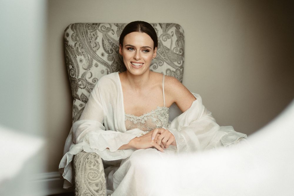 A figure in white bridal attire sits elegantly in a gray upholstered chair.