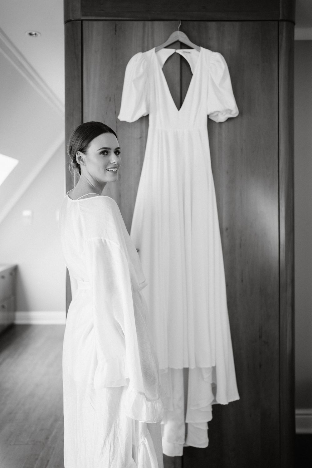 A white wedding dress hanging on display while someone stands nearby in a robe.