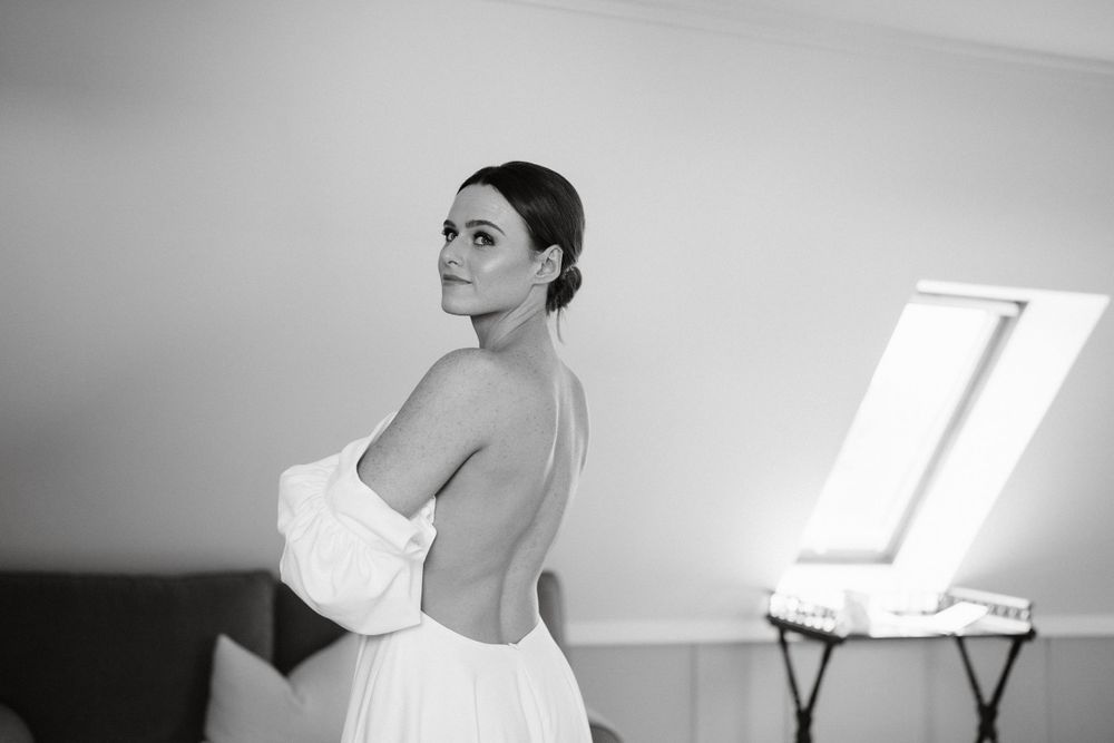 Black and white portrait showing the back of a white wedding dress in natural window light.