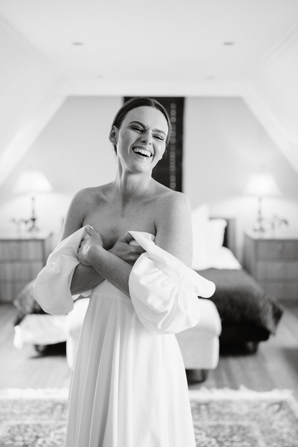 A black and white photograph capturing a joyful moment as someone laughs while wearing an elegant white dress indoors.
