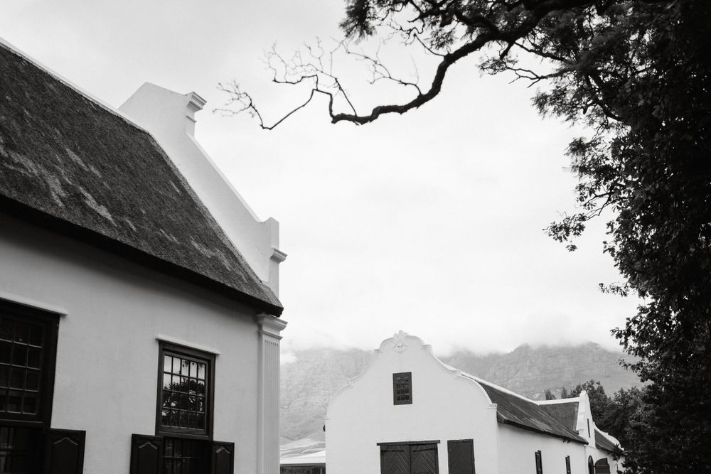 Black and white architectural photo of traditional Cape Dutch style buildings with thatched roofs.