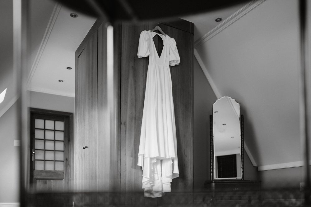 Elegant white wedding dress hanging in a minimalist room captured in black and white photography.