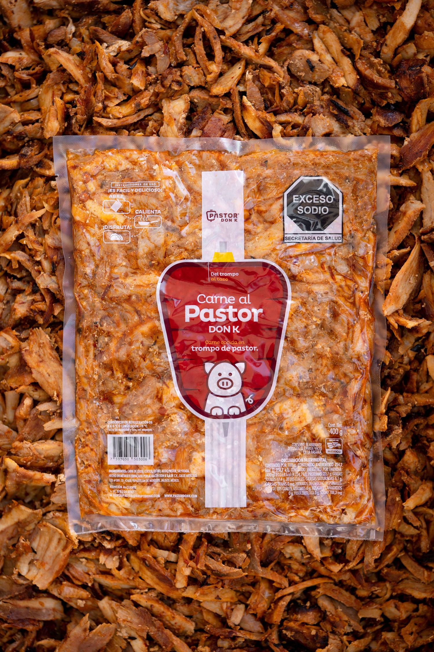 Packaged meat products labeled 'Pastor' displayed on wood shavings background.