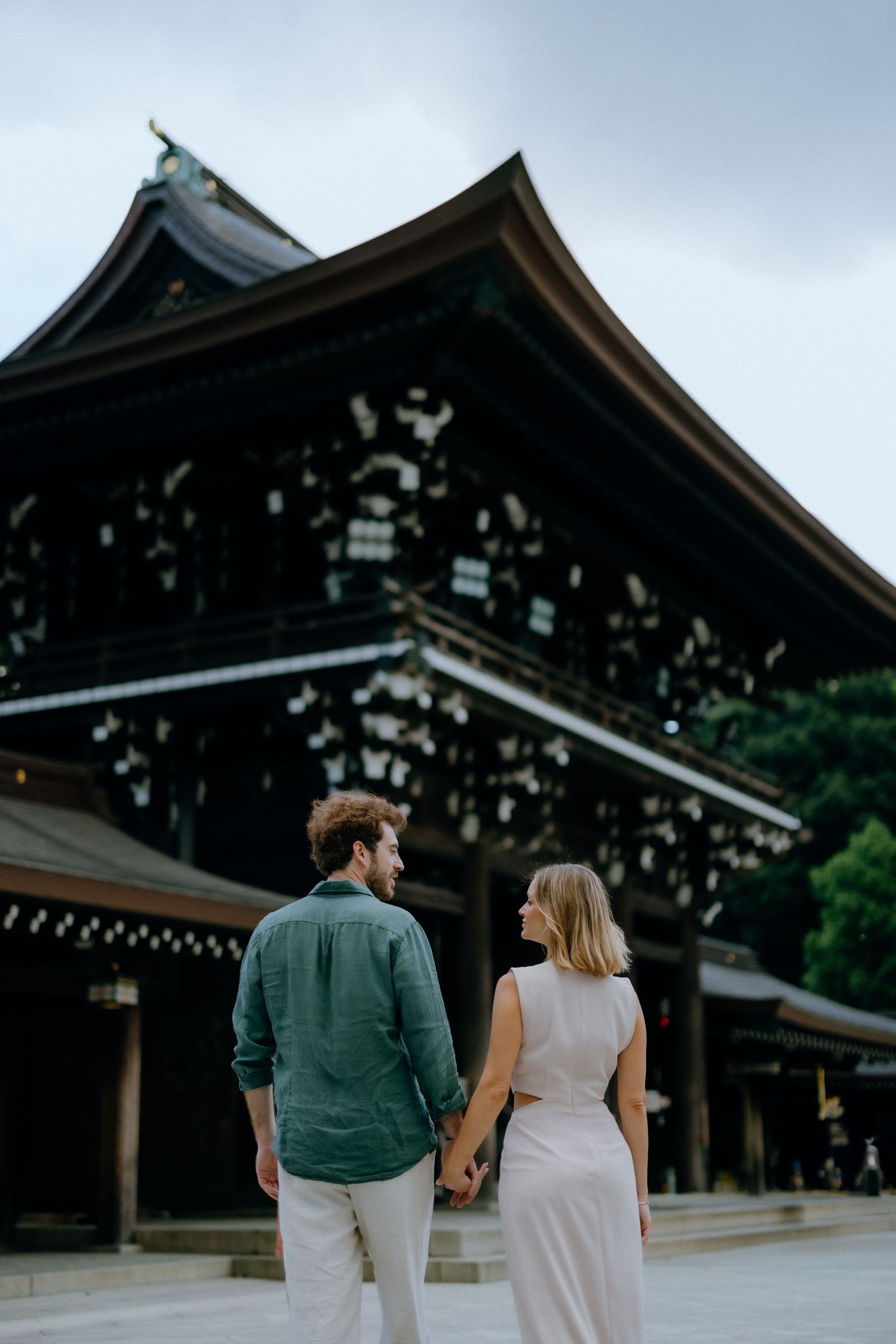 A couple holding hands while walking at a traditional Japanese temple with ornate architecture.