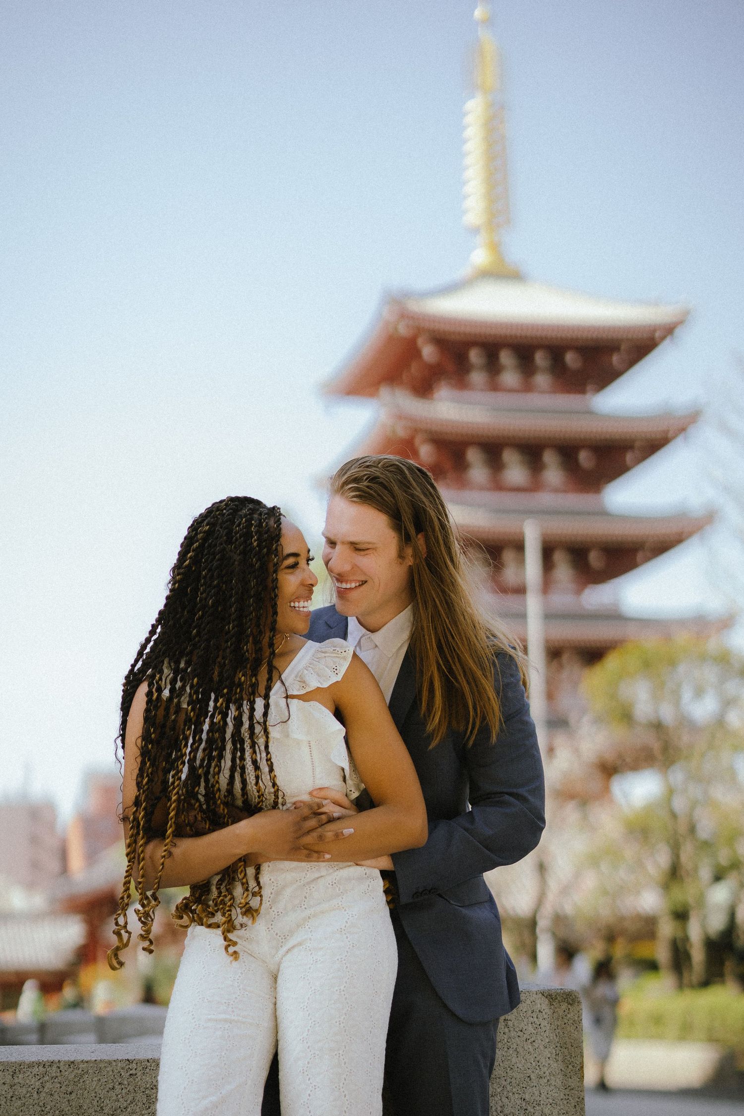 A romantic couple embraces in front of a traditional Japanese pagoda on a bright sunny day.