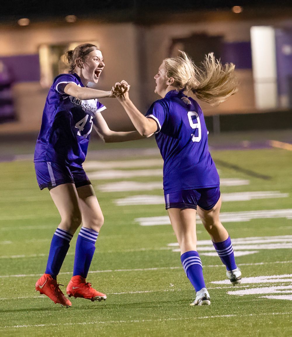 Soccer players in purple uniforms celebrate together with excitement on the field.