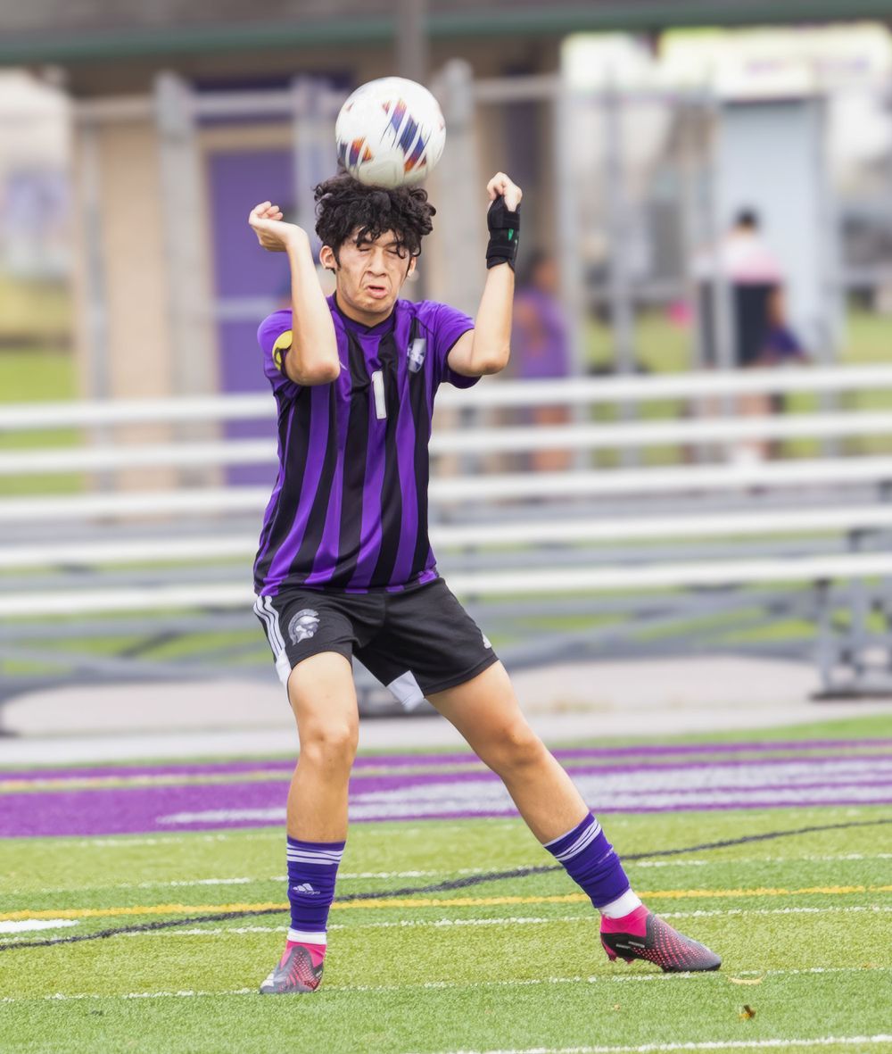 Player in purple striped jersey performs a header during a soccer match.