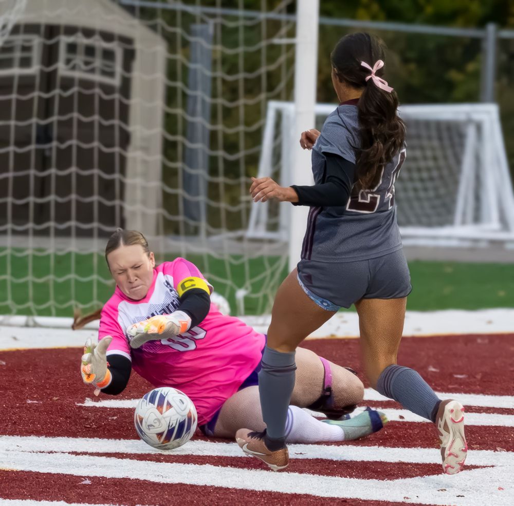 Goalkeeper in pink makes diving save as opponent approaches during soccer match.