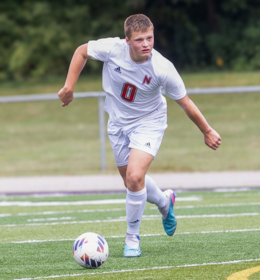 Soccer player in white uniform dribbles ball across field during competitive match.