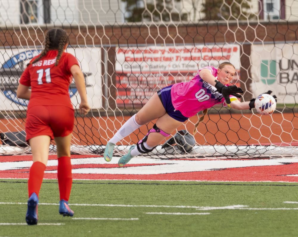 Goalkeeper makes diving save while defending net during soccer match.