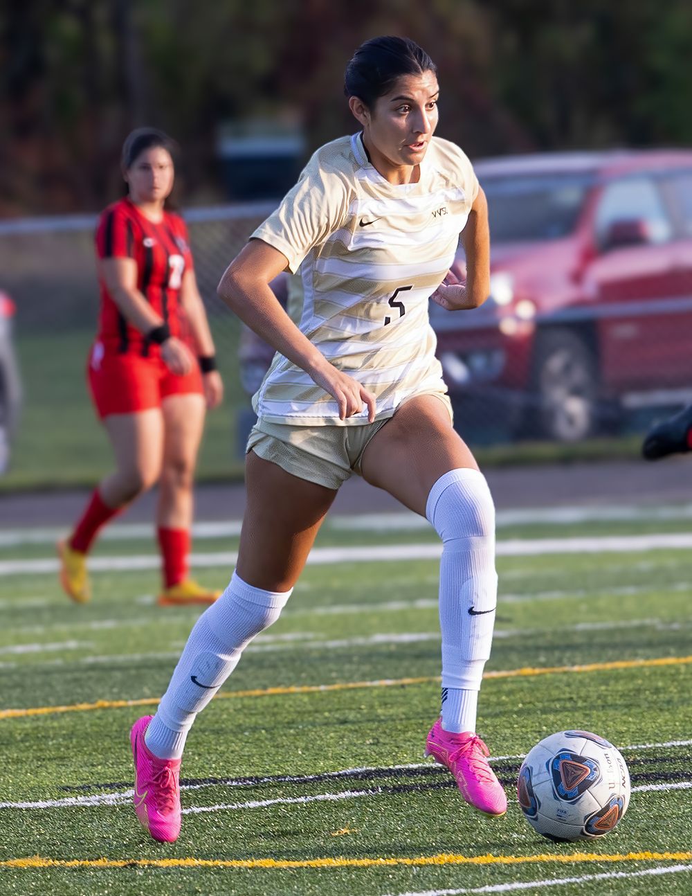 Soccer player in white uniform controls ball during match on turf field.