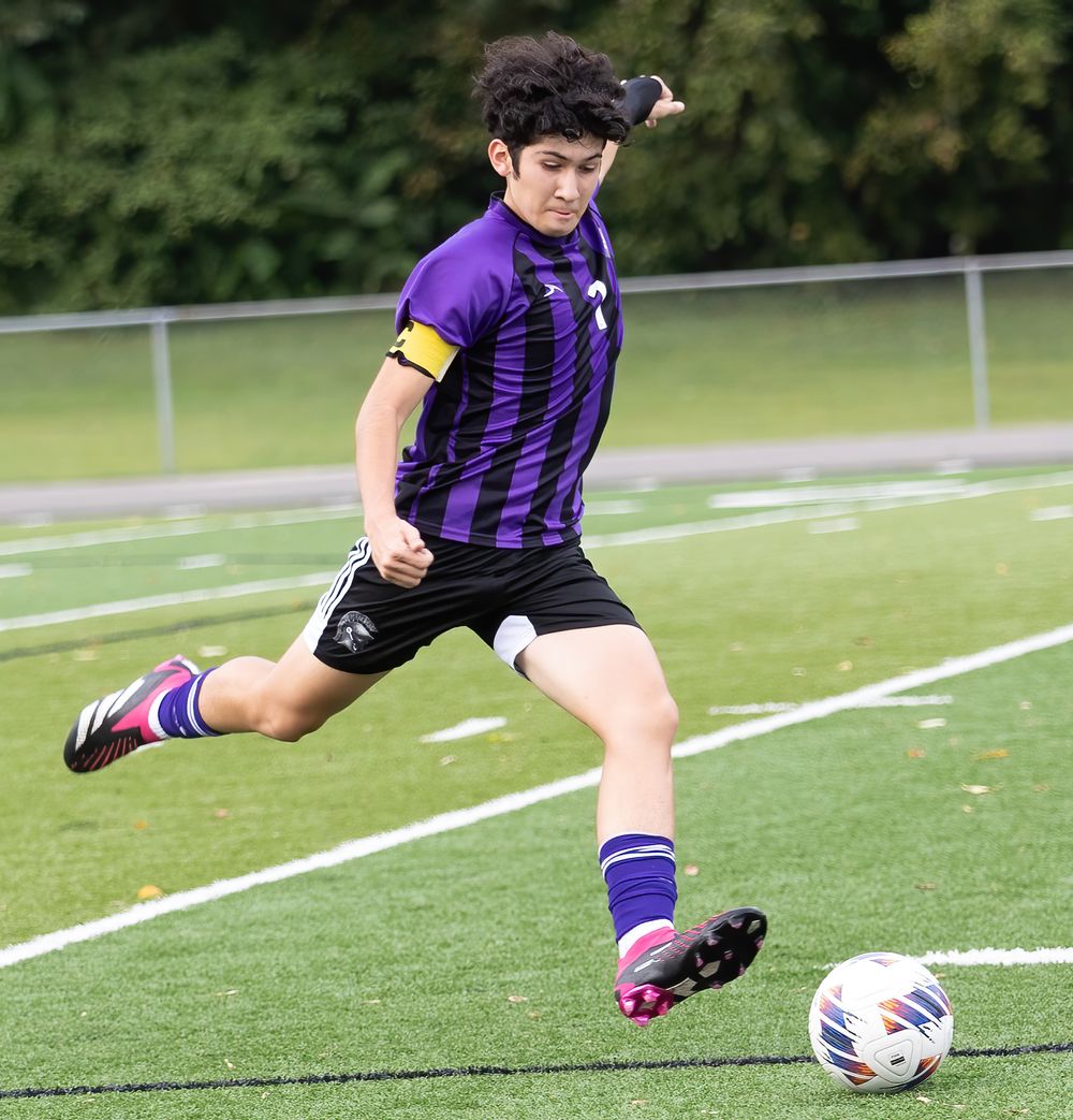 Soccer player in purple striped jersey kicks the ball during a match on an outdoor field.