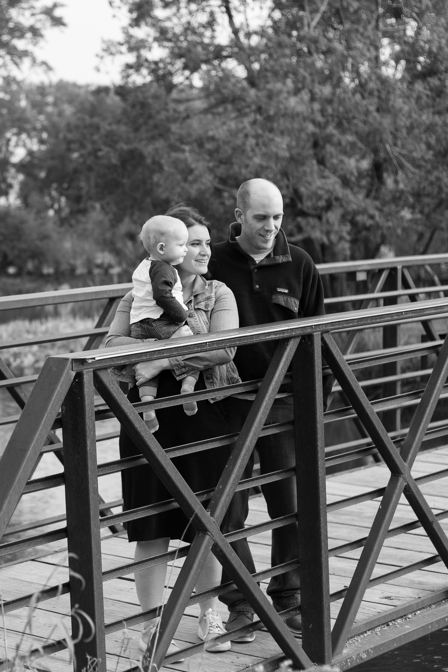 Family looking out from metal bridge railing in black and white portrait.