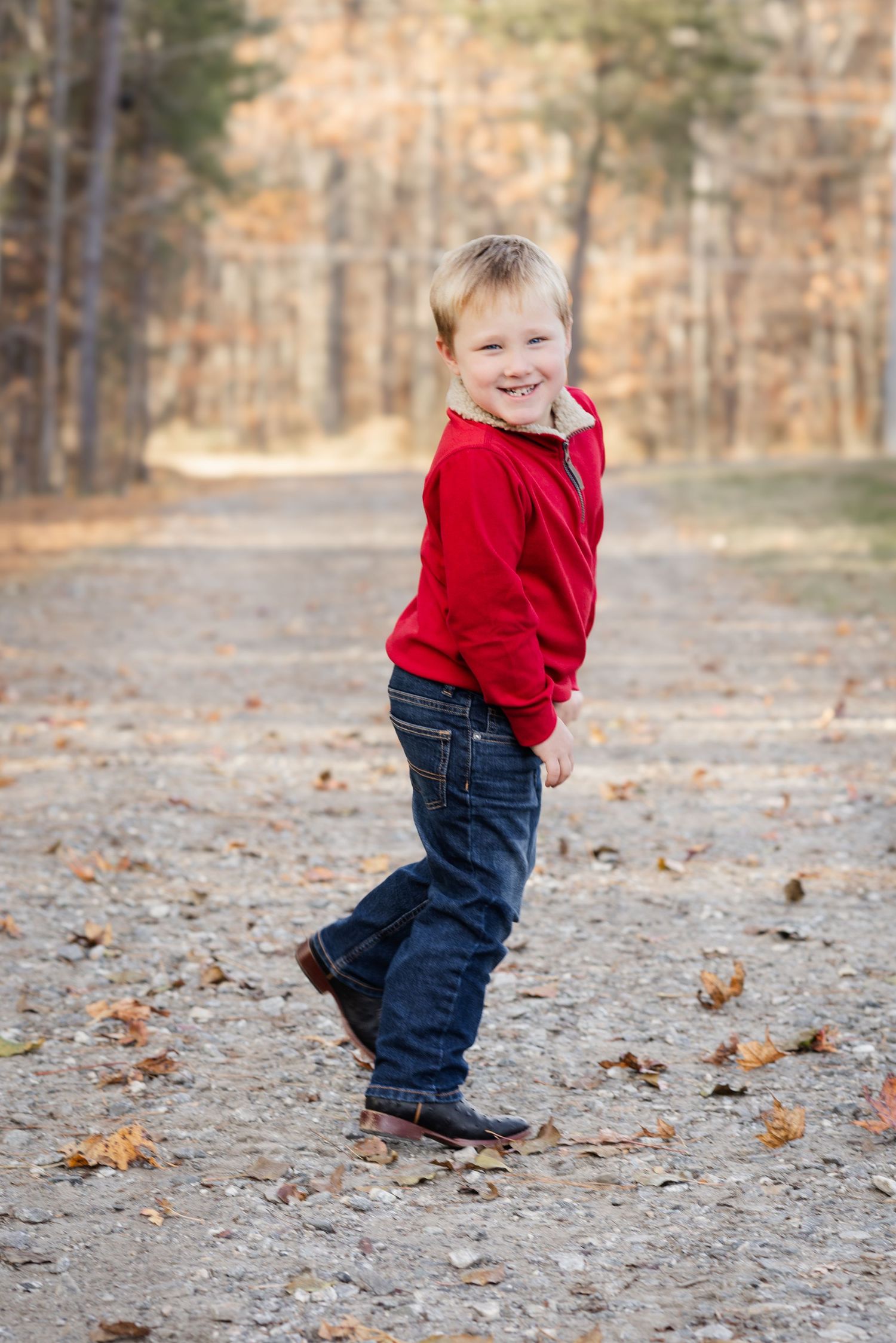 Young child in red hoodie playing on autumn path through woods.