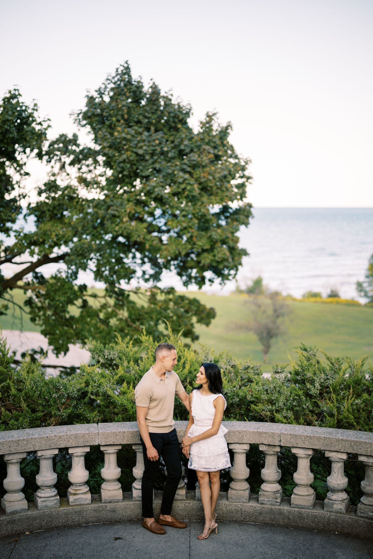 A couple shares an intimate moment on a stone balcony overlooking a scenic waterfront view.